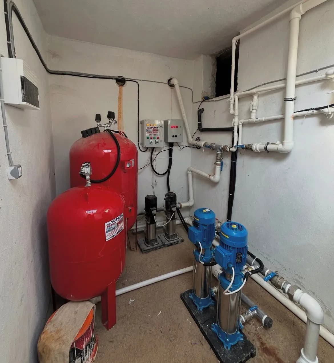 Kırmızı basınç tankı, mavi pompalar ve duvar tipi kontrol panosu